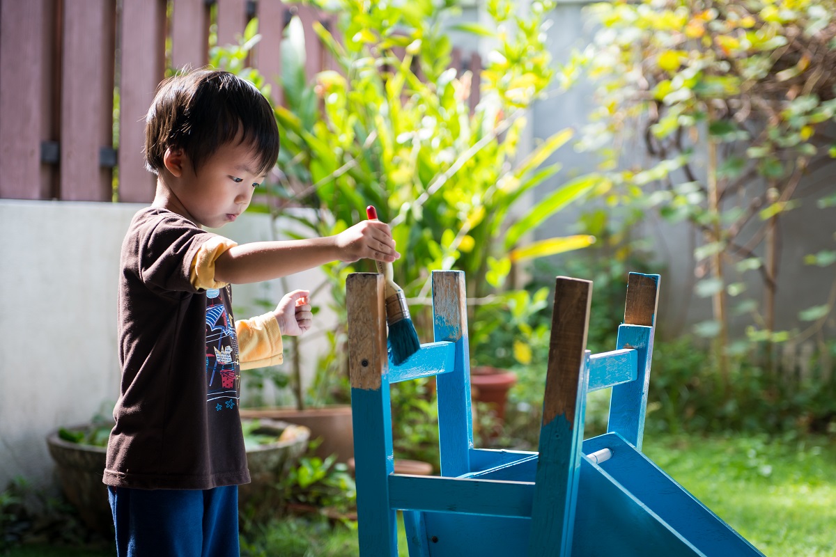 a young boy painting furniture in the garden