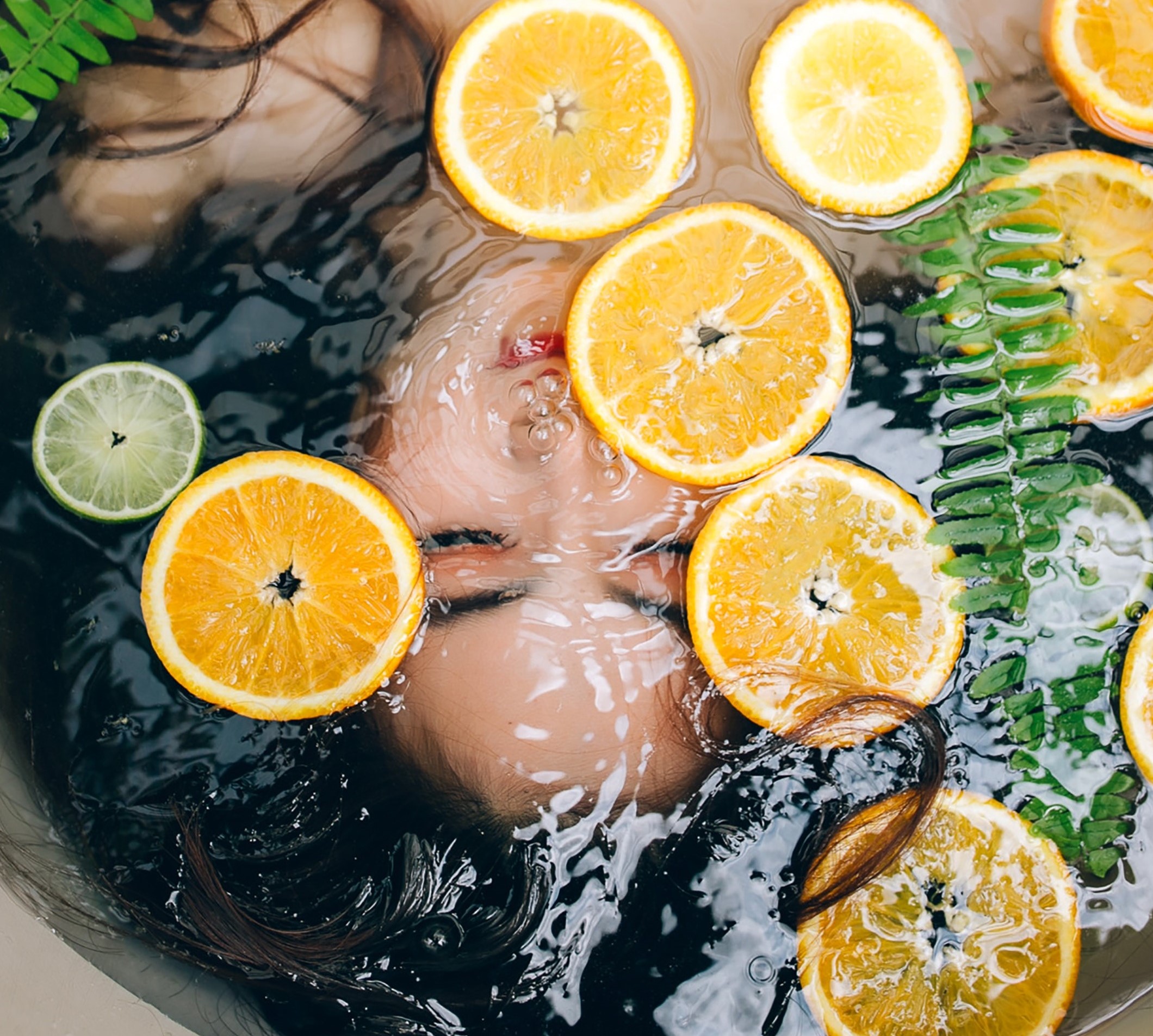 woman's face underwater in tub, with floating citrus fruit slices