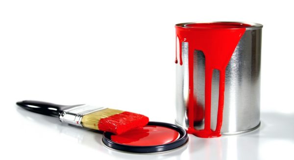 red paint spilling over side of paint can, brush resting on lid