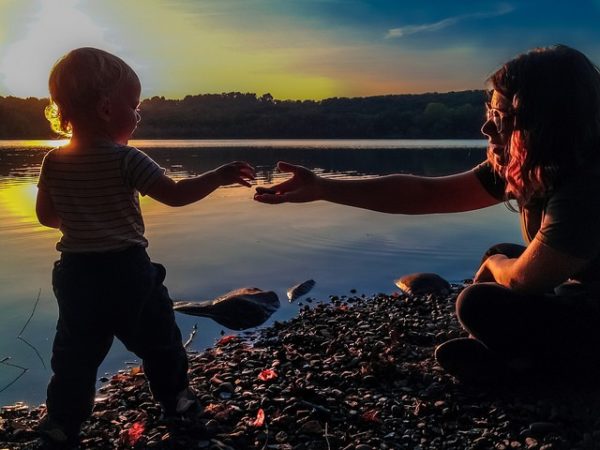 Toddler hands rock to mother along shore