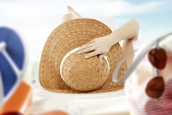 woman laying on beach with sunscreen and beach hat