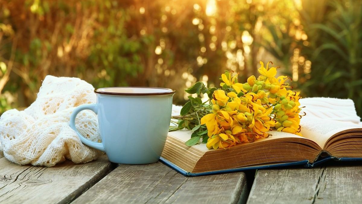 A book, cup, and flowers on wooden table outdoors