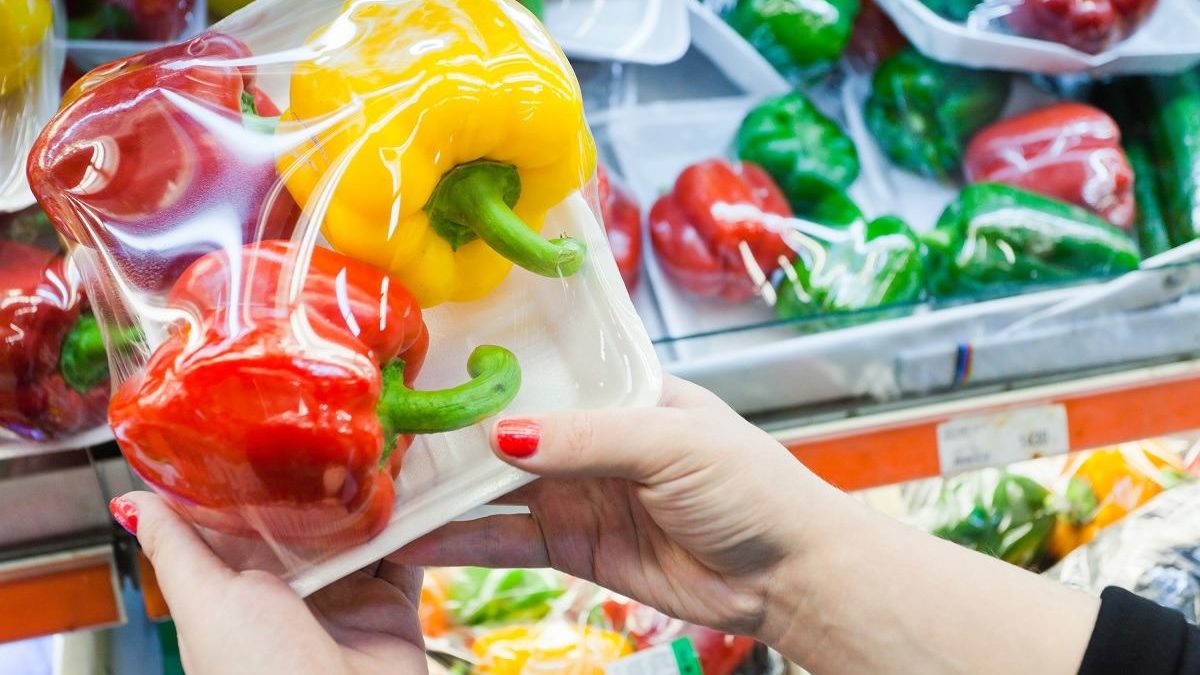 woman's hands holding bell peppers wrapped in plastic