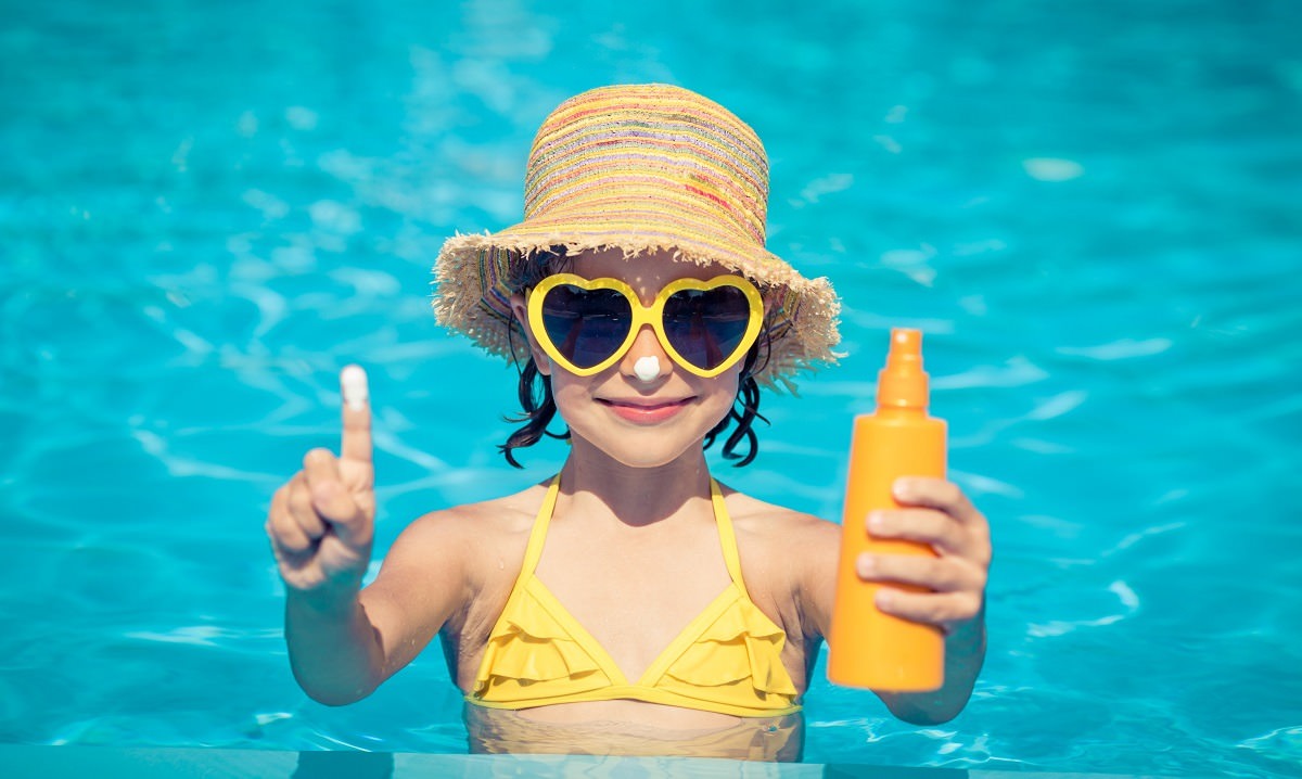 little girl in pool with sunscreen, sunglasses, and hat
