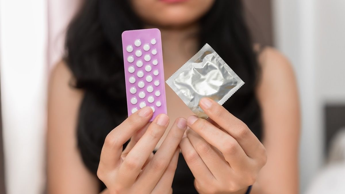 woman holding condom and birth control pills