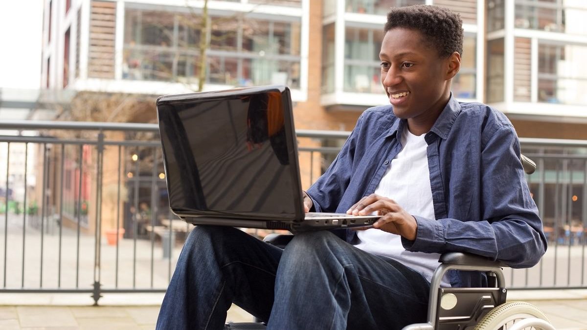 a young wheelchair user working on a laptop outside