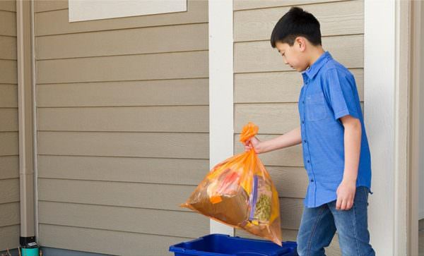 boy placing orange Hefty EnergyBag filled with plastics into recycling bin