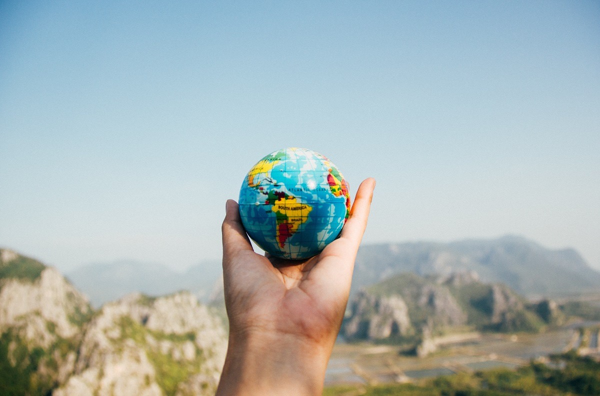 hand holding small globe of world with natural scenery in background