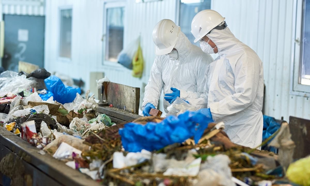 two workers in biohazard suits sorting recyclable materials on conveyor belt