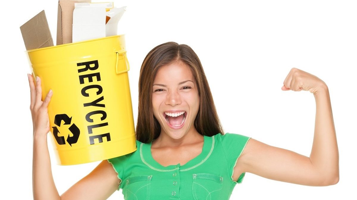 smiling young woman holding recycling bin with paper
