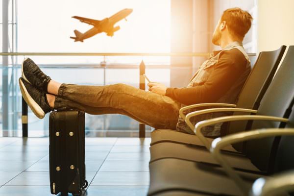young man seated in airport terminal, watching plane take off