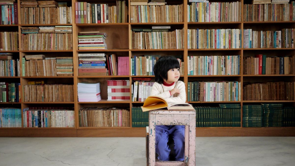 little girl sitting before a full bookshelf