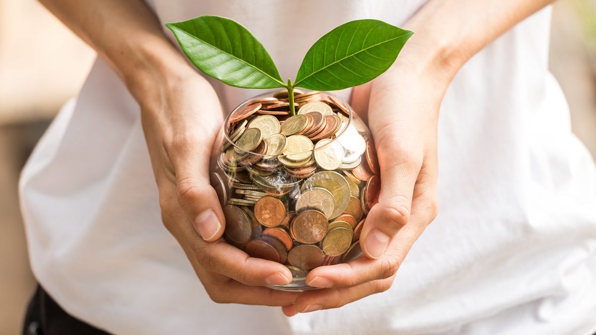 woman's hands holding jar of coins with plant growing out of top