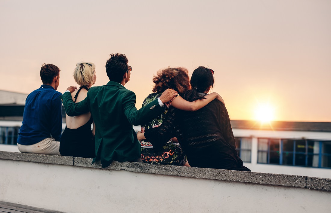 young adults sitting on roof watching sun set