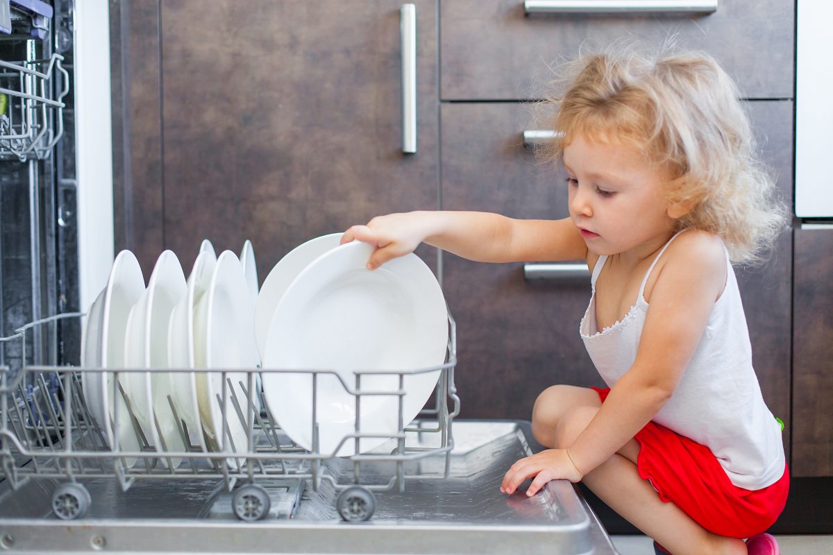toddler girl touching plates in open dishwasher