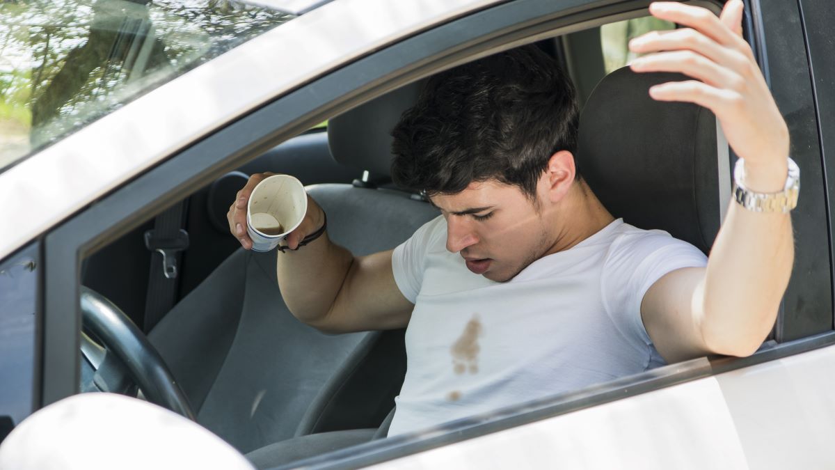 man in car just spilled coffee on white T-shirt