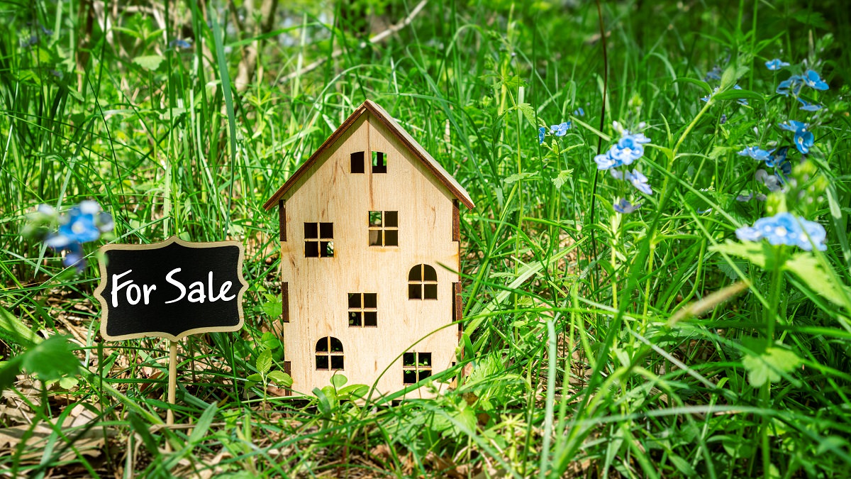 wooden house model with "for sale" sign on grass