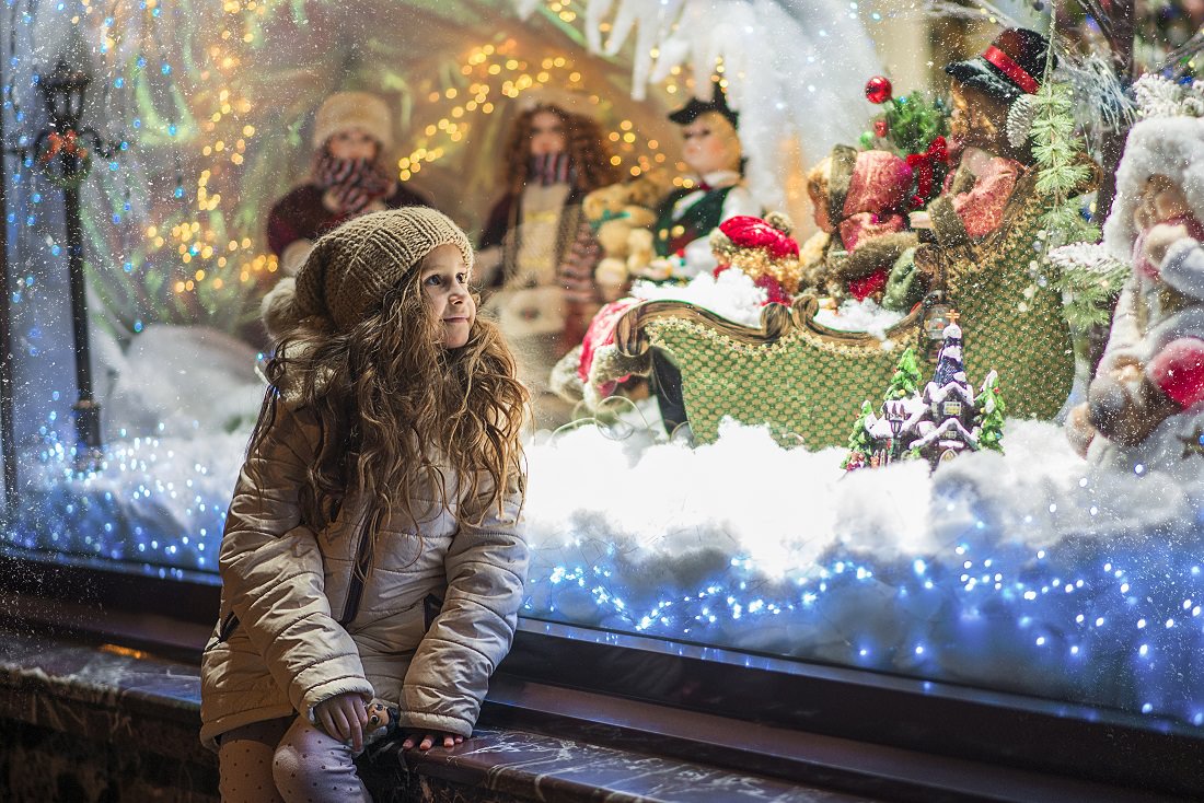 little girl looking store window holiday display