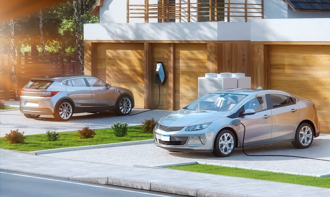 Two electric cars parked and charging in house driveways