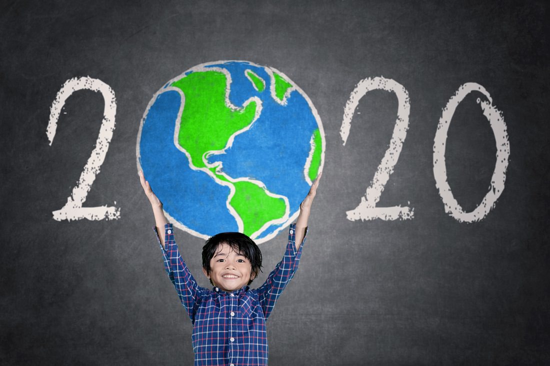 smiling boy lifting globe in front of "2020" on chalk board