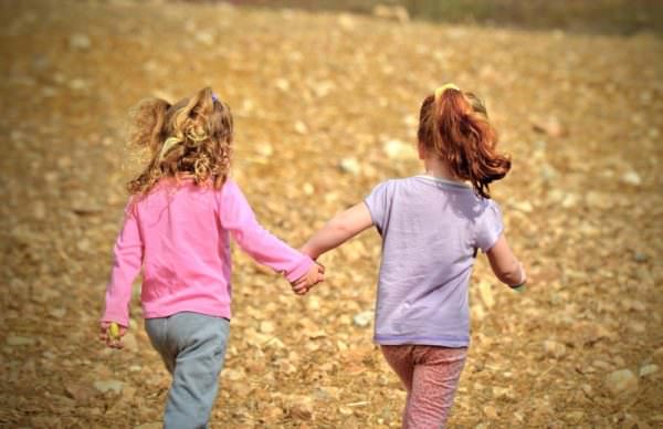 two young girls holding hands and walking in open space