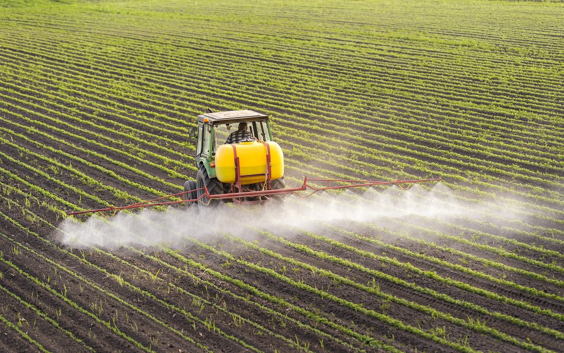 tractor spraying pesticides on soybean crop