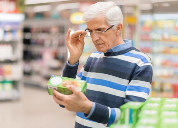 white-haired man reading food label in grocery store