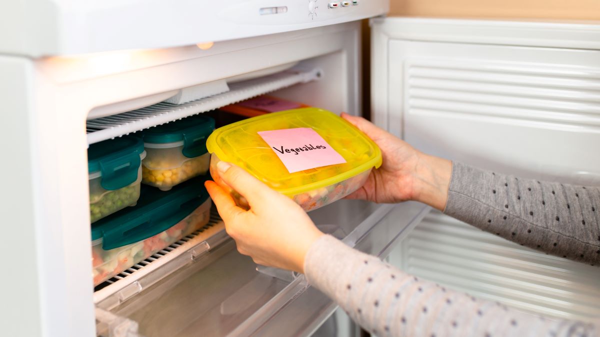 woman putting container of frozen vegetables into freezer