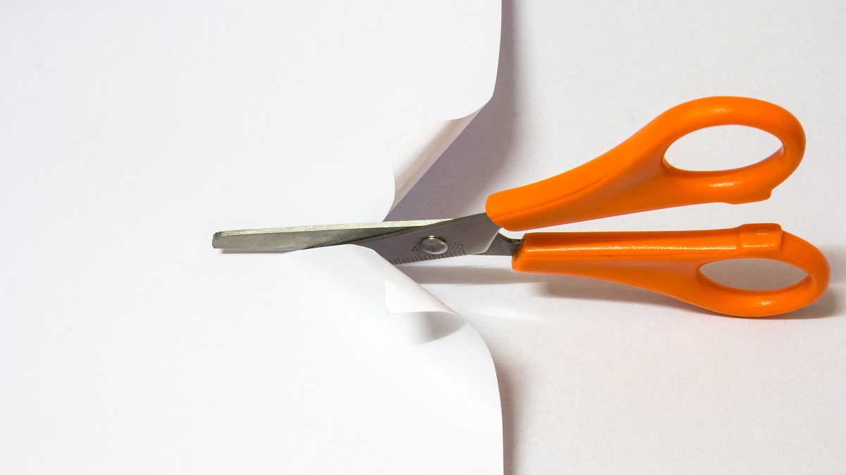 Orange handled scissors cutting white paper on white background