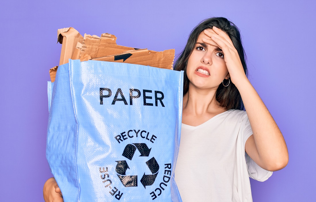 woman holding bag of paper to recycle, looks upset