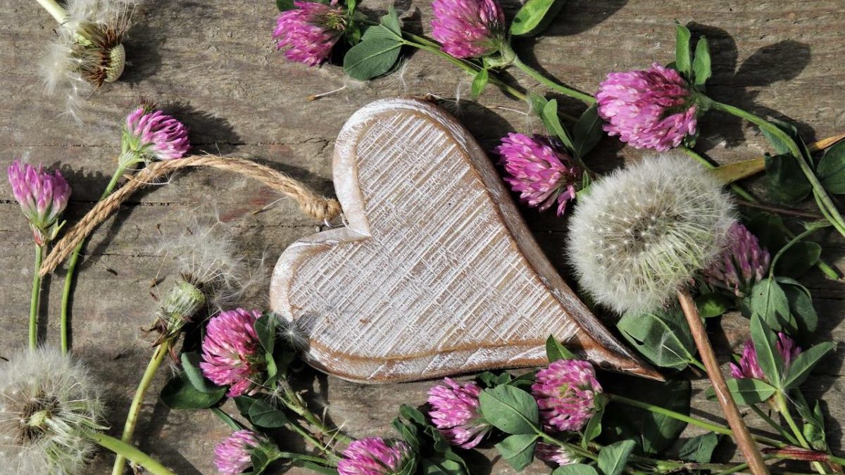 wooden heart surrounded by clover and dandelion flowers