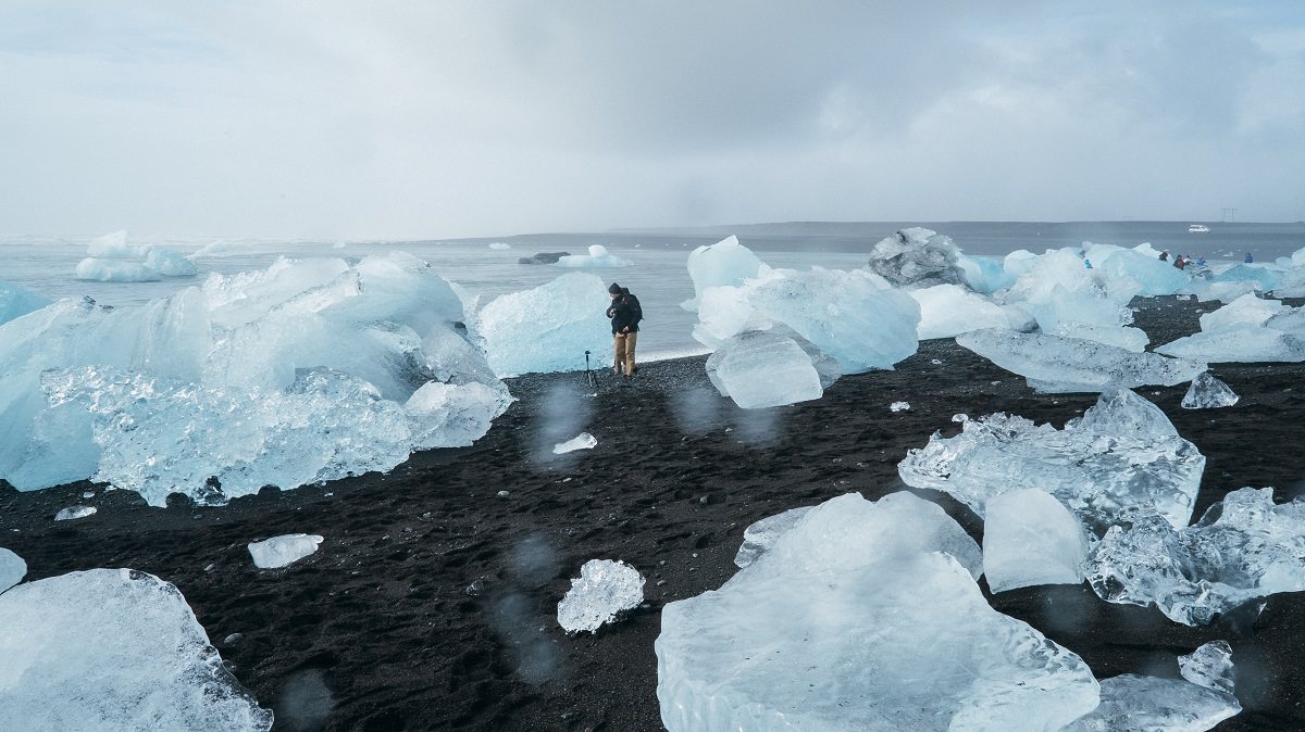 person standing on bare earth next to melted glacier