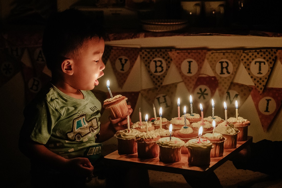 little boy blowing out birthday candle on cupcake