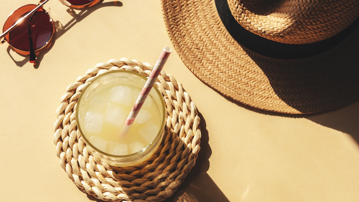 A glass with iced lemonade, hat, and sunglasses