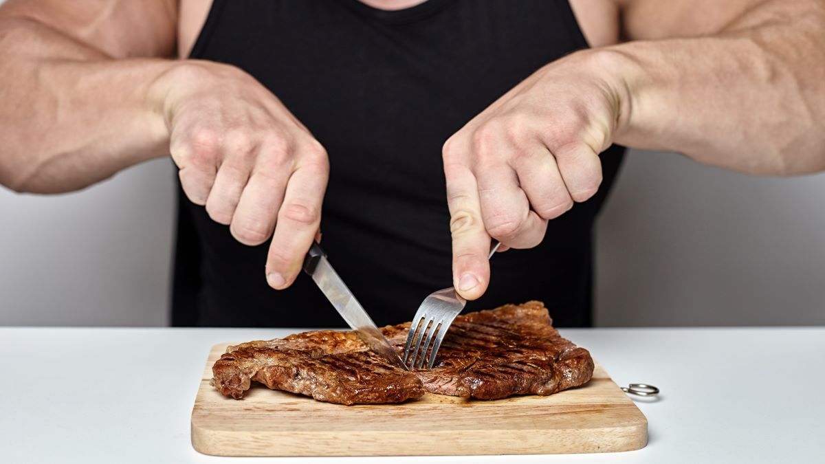 close up of man's hands cutting beef steak on wood cutting board