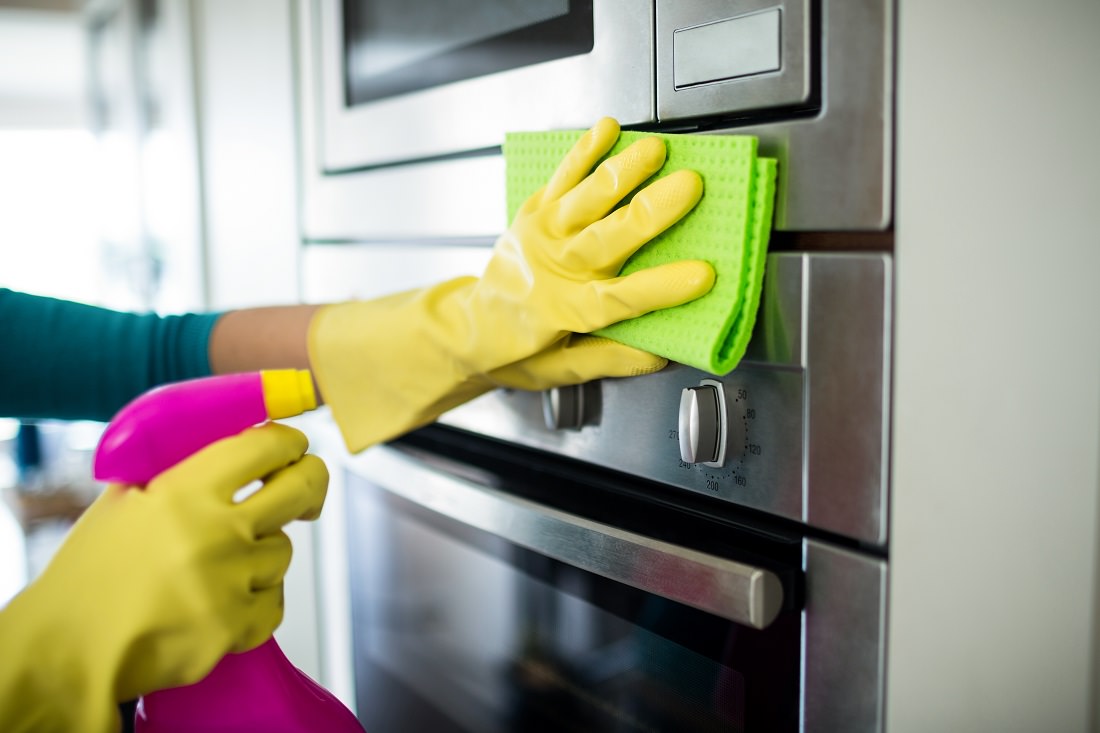 close-up of hands wearing kitchen gloves and cleaning oven