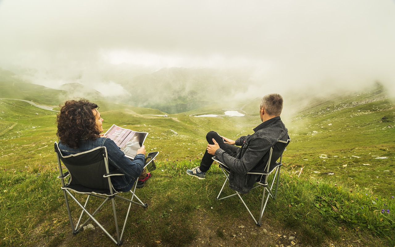 A couple sitting on green hillside in camp chairs