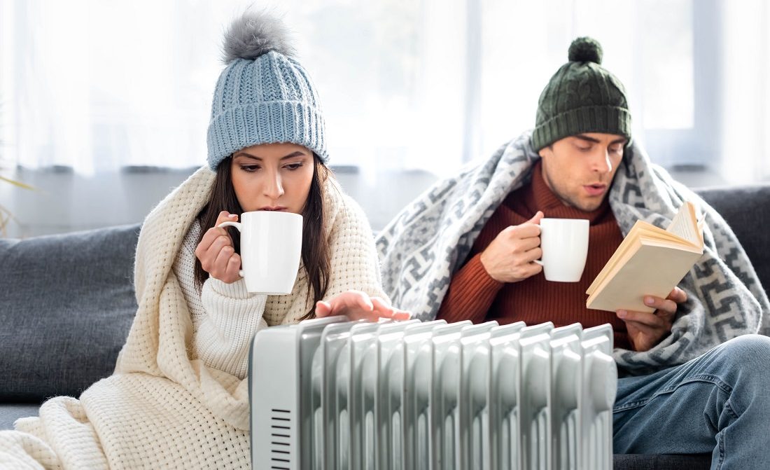 young couple bundled up and getting warm near heater
