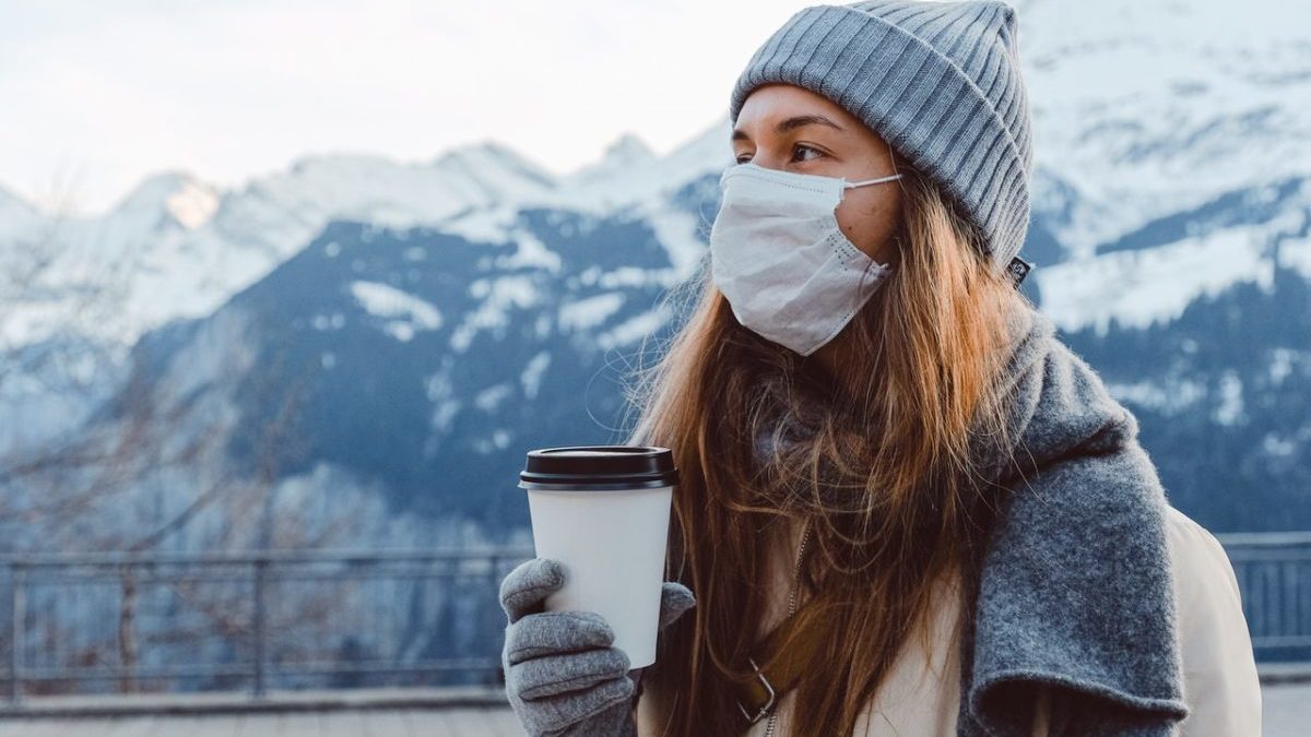 woman in disposable mask holding single-use coffee cup with plastic lid