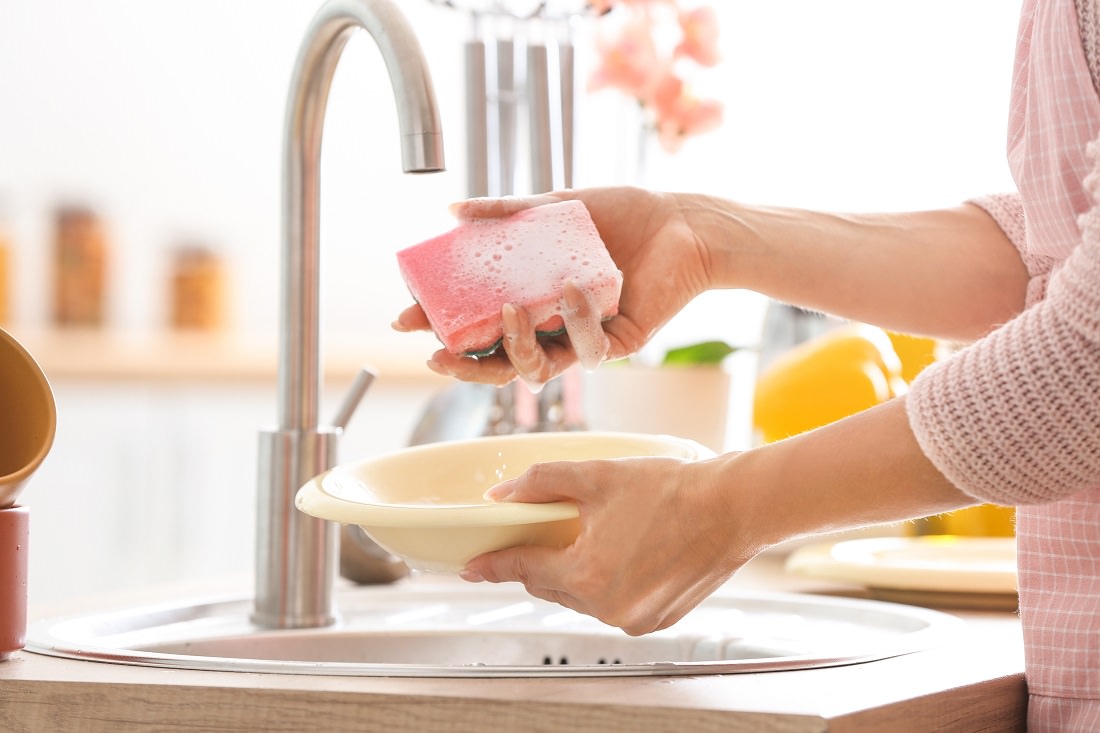 Close-up of woman's hands holding soapy sponge and dish over sink