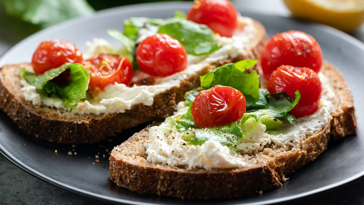 Toast with soft ricotta cheese, roasted tomatoes and lettuce garnished with olive oil and black pepper.