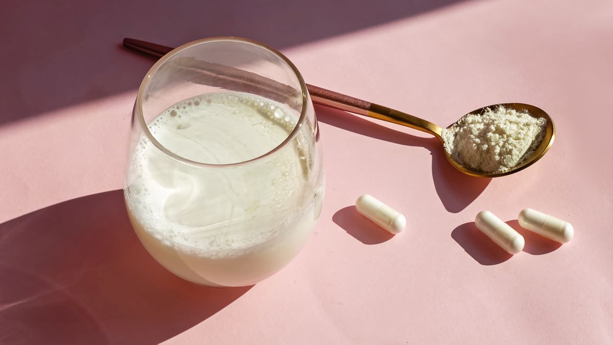collagen supplement in powder and pill in spoon next to glass of milk