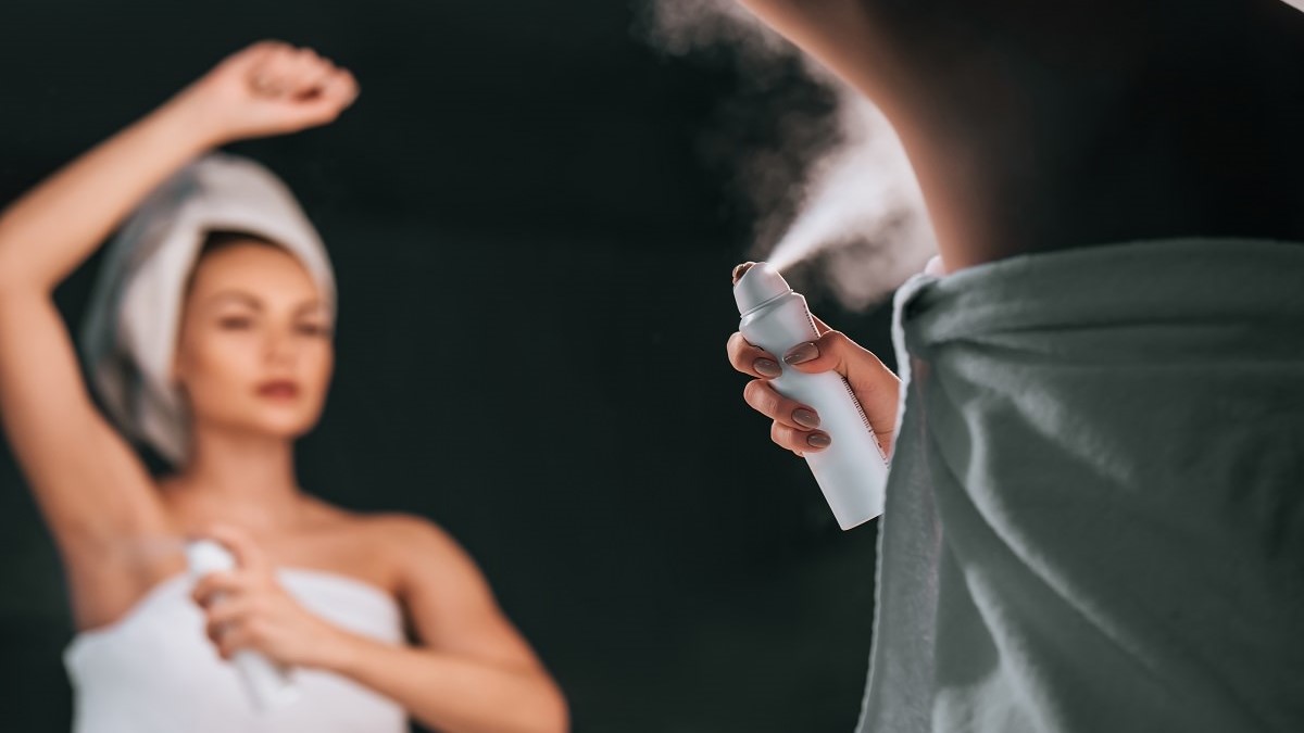 woman wrapped in towel spraying deodorant