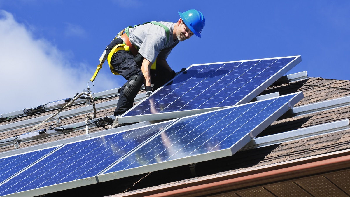 Man installing alternative energy photovoltaic solar panels on house roof