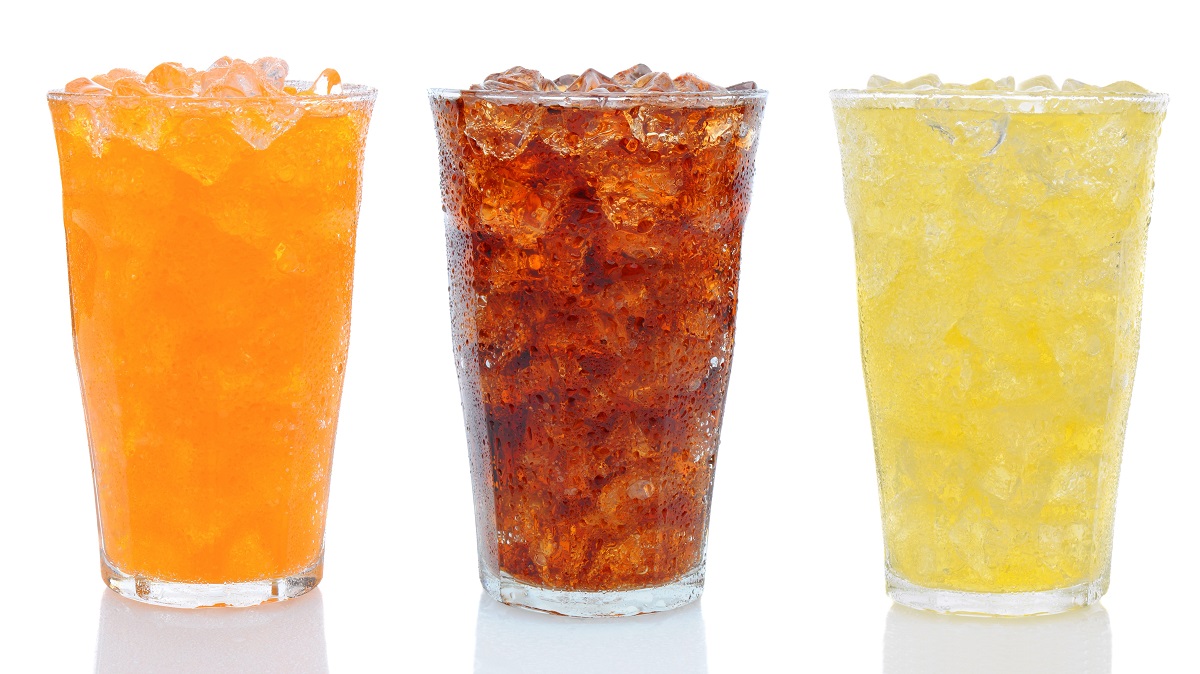 Closeup of three glasses of soda, Cola, Orange and Lemon Lime on white with reflection. Filled with ice the glasses are covered with condensation