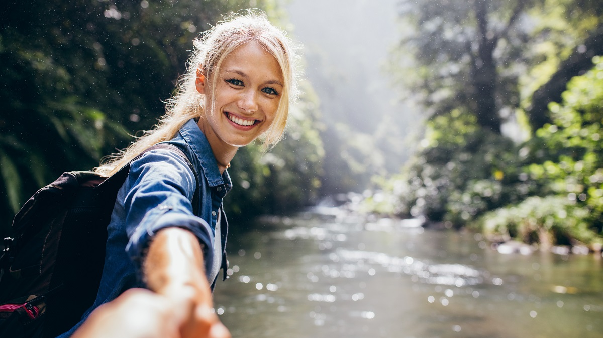 Beautiful smiling young woman on hike by stream