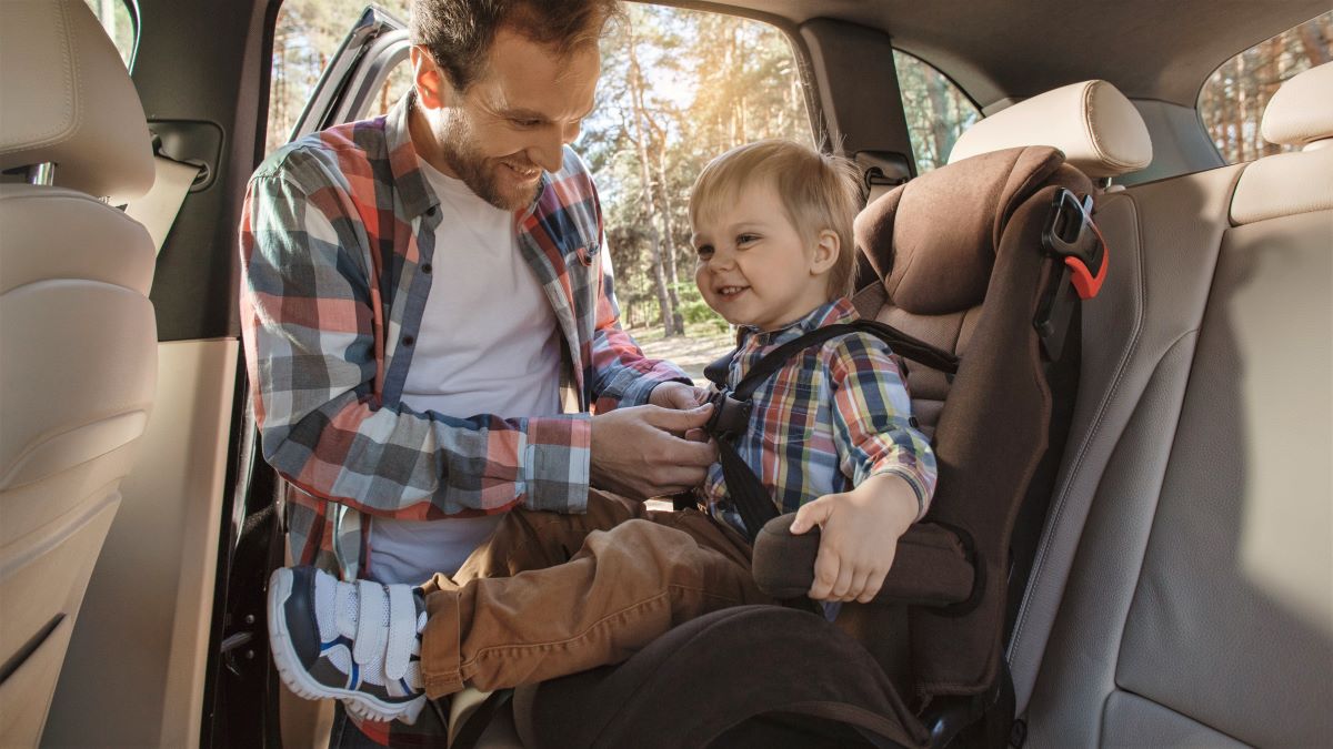 Man buckling little boy into his car seat
