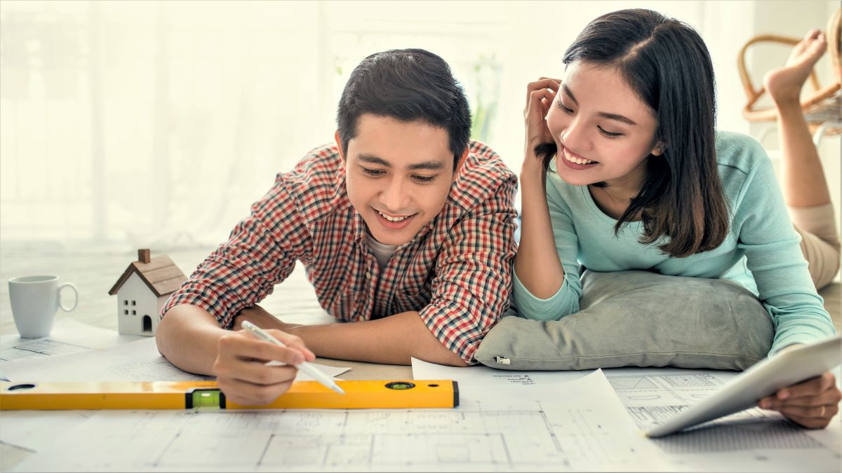 young man and woman on floor looking at blueprints of new home