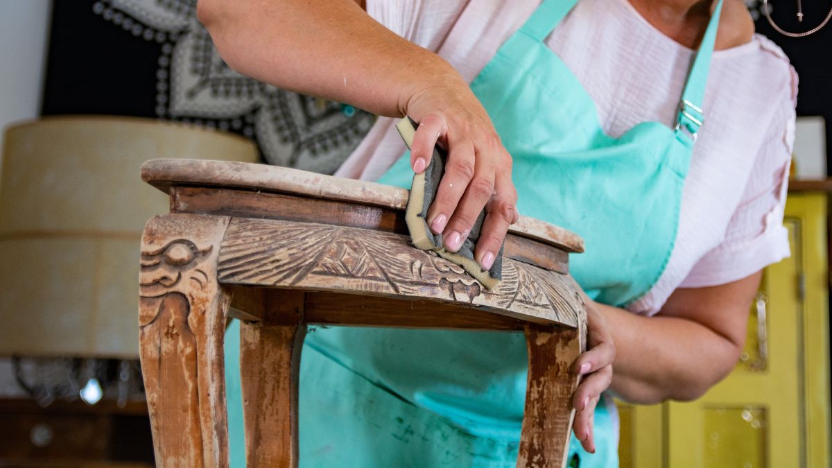 woman restoring old wooden side table with intricate carving