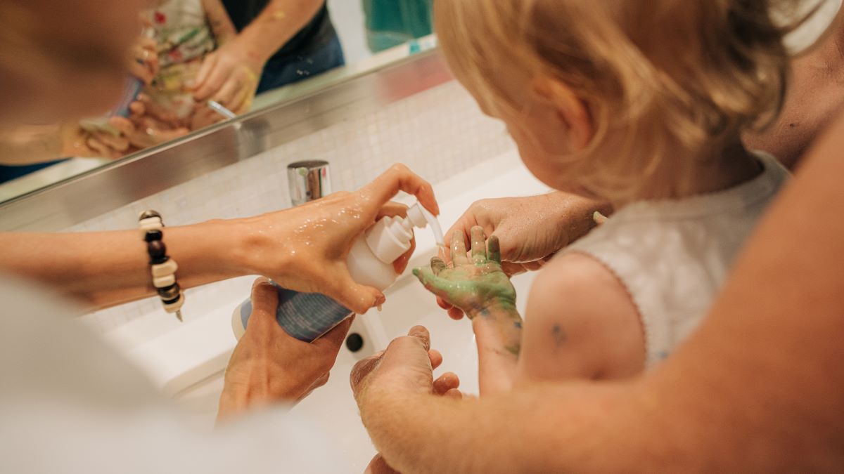 Two adults washing child's hand with liquid hand soap